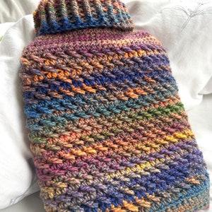 May include: A colourful crocheted hot water bottle with a diagonal pattern in shades of blue, orange, brown, and purple.