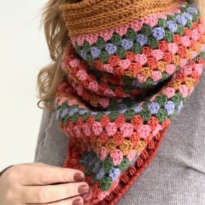Puede incluir: Una bufanda de ganchillo colorida con rayas de color rosa, verde, azul y naranja. La bufanda está hecha con un punto de granny square.