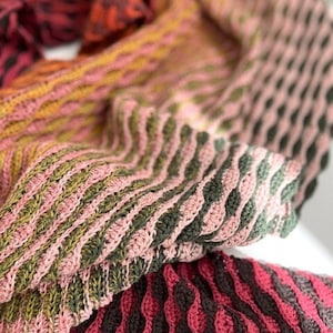 May include: A crocheted scarf in shades of pink, green, and brown. The scarf is made with a variety of stitches and has a textured look.