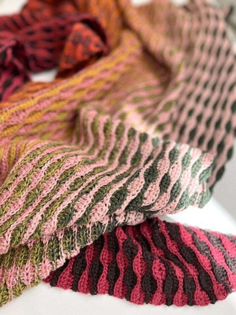 May include: A crocheted scarf in shades of pink, green, and brown. The scarf is made with a variety of stitches and has a textured look.