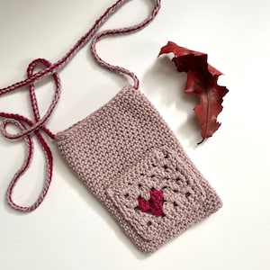 May include: A small pink crocheted bag with a heart-shaped design in the front pocket. The bag has a long strap for carrying over the shoulder.