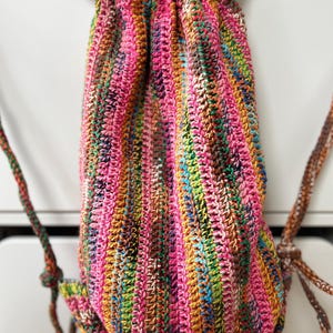 May include: A colorful crocheted drawstring bag with a pink, green, brown, and yellow striped pattern.