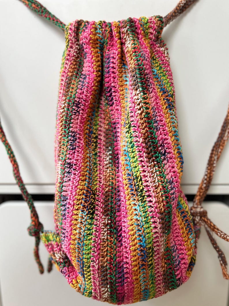 May include: A colorful crocheted drawstring bag with a pink, green, brown, and yellow striped pattern.