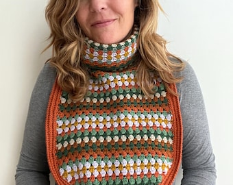 May include: A crocheted cowl with a multi-coloured striped pattern in shades of orange, green, white, and brown. The cowl has a rounded shape and a contrasting orange border.