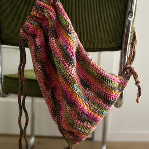 Op de afbeelding: Een kleurrijke gestreepte gehaakte trekkoordtas met een lang, geknoopt koord.