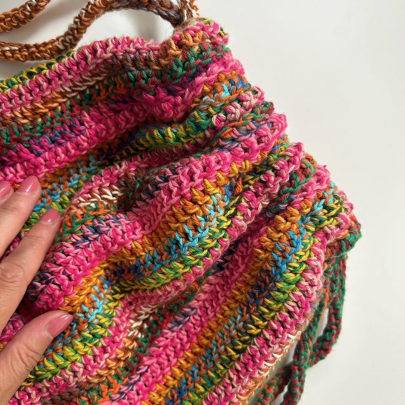 May include: A colorful crocheted drawstring bag with a pink, orange, green, and blue striped pattern.