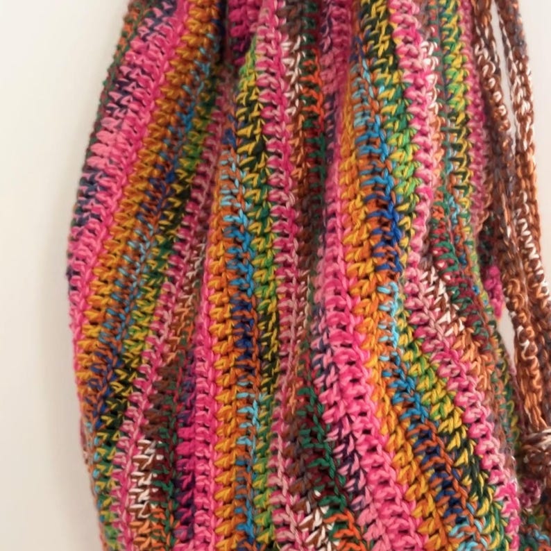 May include: A close-up of a colorful crocheted bag with a striped pattern in shades of pink, orange, brown, green, and blue.