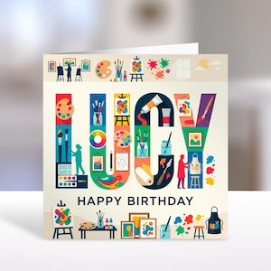 May include: A square greeting card with a cream background featuring the name LUCY in large, colourful letters filled with art-themed illustrations like paint palettes, brushes, and easels. Below the name, the text reads HAPPY BIRTHDAY.