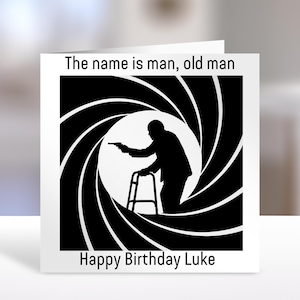 May include: A square greeting card with a white background and a black and white graphic. The graphic shows a silhouette of a person with a walker holding a gun inside a circular gun barrel design. Text reads: The name is man, old man. Happy Birthday Luke.