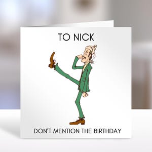 May include: A square greeting card with a white background featuring the text TO NICK at the top and DON'T MENTION THE BIRTHDAY at the bottom. In the centre is a cartoon illustration of a person in a green suit and brown shoes kicking a leg.