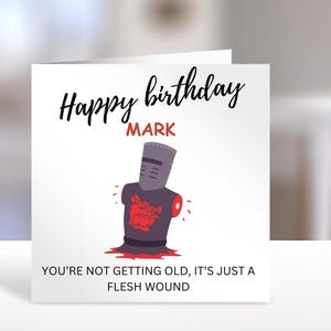 May include: A square greeting card with a white background featuring the text Happy birthday MARK in black and red. Below is a graphic of a dark grey knight helmet and torso with a red boar emblem, and the text YOU'RE NOT GETTING OLD, IT'S JUST A FLESH WOUND.