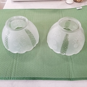 Peut inclure: Deux abat-jours en verre assortis avec une finition dépolie. Chaque abat-jour présente un bord festonné, une ouverture circulaire au sommet et des panneaux alternés de motifs floraux gravés et une texture en losange en relief.