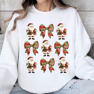 Op de afbeelding: Witte sweatshirt met een herhaald patroon van kerstmanfiguren en decoratieve strikken. De kerstmanfiguren dragen rode en groene outfits, terwijl de strikken rode, groene en witte patronen hebben. Een feestelijk ontwerp voor de feestdagen.
