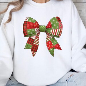 Puede incluir: Sudadera blanca con un gran diseño de lazo colorido. El lazo está compuesto por patrones de patchwork en rojo, verde y blanco, con lunares, rayas y motivos festivos navideños como copos de nieve y hombres de jengibre.