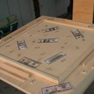 May include: A wooden game table with a light wood finish. The table top has a raised border and is decorated with dollar bills. The table has a built-in drawer.