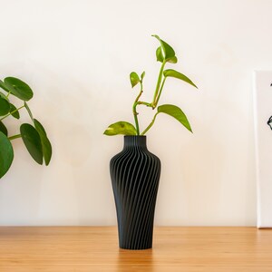 Peut inclure: Un vase en céramique noir ondulé avec une seule tige de feuilles vertes.