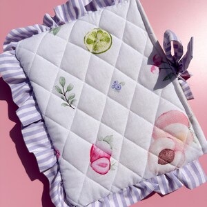 Puede incluir: Tela acolchada blanca con un patrón de diamantes, con ilustraciones de acuarela de una rodaja de lima, fresa y acentos florales. Los bordes están adornados con un borde con volantes en un patrón de rayas lavanda y blanco. Se adjunta un lazo lavanda.