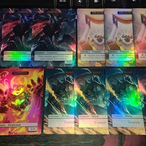 May include: A collection of ten Magic: The Gathering cards featuring various creatures and artifacts. The cards are holographic and have a rainbow sheen. The cards include "Construct", "Elemental", "Rhino", and "Treasure".