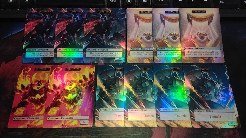 May include: A collection of ten Magic: The Gathering cards featuring various creatures and artifacts. The cards are holographic and have a rainbow sheen. The cards include "Construct", "Elemental", "Rhino", and "Treasure".