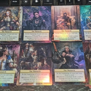 May include: Eight holographic playing cards with a rainbow sheen. Each card features a different character in a regal pose and the text "The Monarch" with the following text: "At the beginning of your end step, draw a card. Whenever a creature deals combat damage to you, its controller becomes the monarch."
