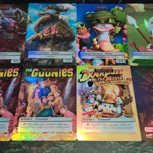 May include: A set of nine trading cards featuring characters from popular films, including "The Goonies" and "DuckTales: The Movie - Treasure of the Lost Lamp". The cards are holographic and have a colourful, cartoon-like style.