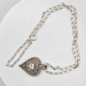 May include: A silver necklace with a heart-shaped pendant featuring a clear rhinestone. The chain is a delicate, linked design.