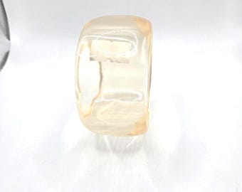 Könnte beinhalten: Ein durchsichtiges, hellpfirsichfarbenes Armreif-Armband. Der Armreif ist glatt und hat eine abgerundete Form.