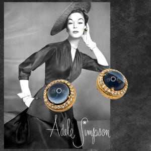 May include: A pair of gold tone earrings with a blue cabochon stone set in a round bezel. The stones are surrounded by a halo of clear rhinestones.