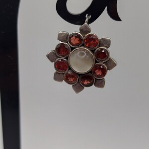 May include: Silver earring with a white pearl center and red gemstones around it.