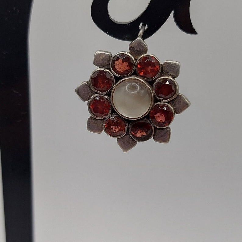 May include: Silver earring with a white pearl center and red gemstones around it.