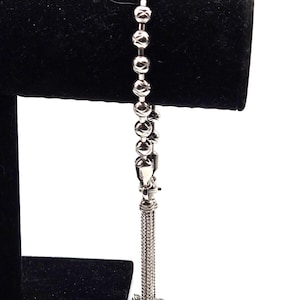 Könnte beinhalten: Ein silbernes Armband mit einer Kette und einem Quastenanhänger. Die Kette besteht aus kleinen, runden Perlen.