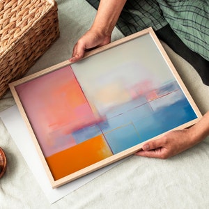 Könnte beinhalten: Ein gerahmtes abstraktes Gemälde mit einem Farbschema aus Hellblau, Orange und Rosa. Das Gemälde ist in einem Holzrahmen und wird von einer Person gehalten.