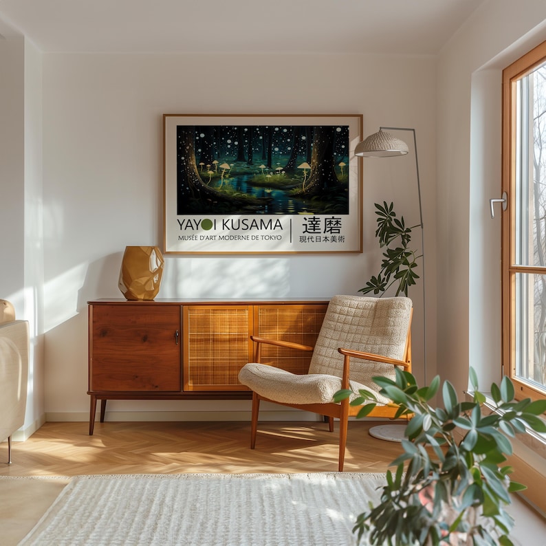May include: A poster with a forest scene in shades of green and blue with white dots. The poster is titled "Yayoi Kusama" and features the text "Mus&eacute;e d'Art Moderne de Tokyo" and "草間彌生" in Japanese. The poster is hanging on a white wall in a living room with a wooden cabinet and a chair.