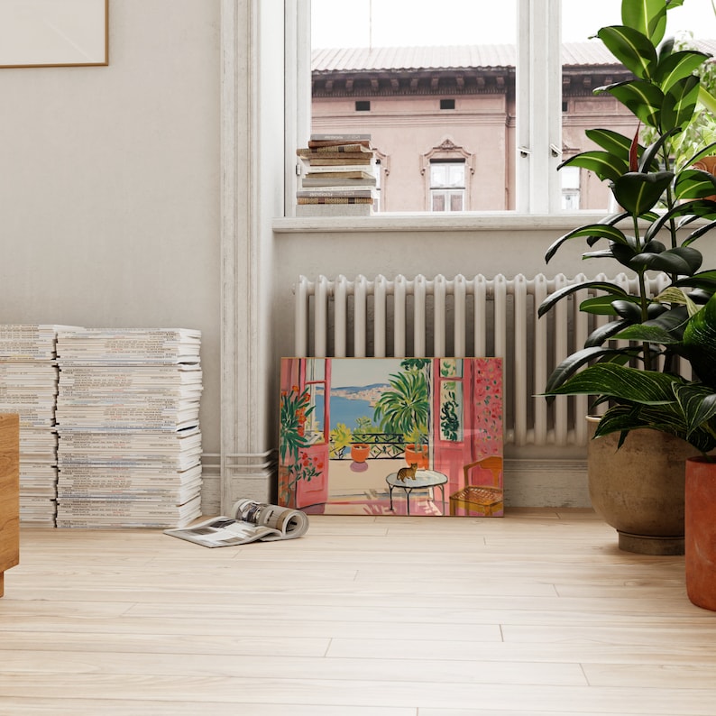 Puede incluir: Una pintura enmarcada de una habitaci&oacute;n rosa con una ventana abierta que da a un mar azul y una ciudad. La habitaci&oacute;n tiene una mesa con una silla y una planta en maceta. La pintura est&aacute; en un marco de madera claro.