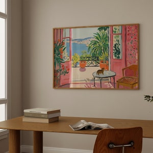 Puede incluir: Una pintura enmarcada de una habitaci&oacute;n rosa con una ventana que da a una masa de agua azul. La ventana est&aacute; abierta y hay un gato sentado en una mesa en la habitaci&oacute;n. La pintura est&aacute; en un marco de madera.