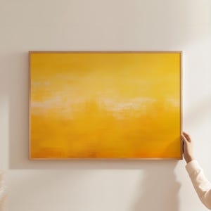 May include: A framed abstract painting with a yellow and white colour scheme. The painting has a soft, blurred effect, creating a sense of movement and depth.