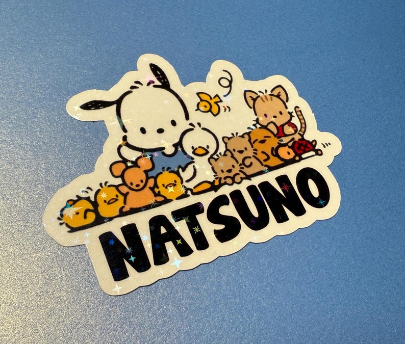 Puede incluir: Una pegatina blanca con un perro de dibujos animados y otros animales. La pegatina tiene un acabado brillante y dice "NATSU NO" en letras negras.