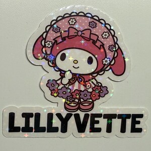 May include: A pink and white cartoon character with a pink bow and a pink and white dress with purple flowers. The character is wearing a pink and white hat with a white trim. The character is standing on a white background with the text "LILLYVETTE" in black letters.