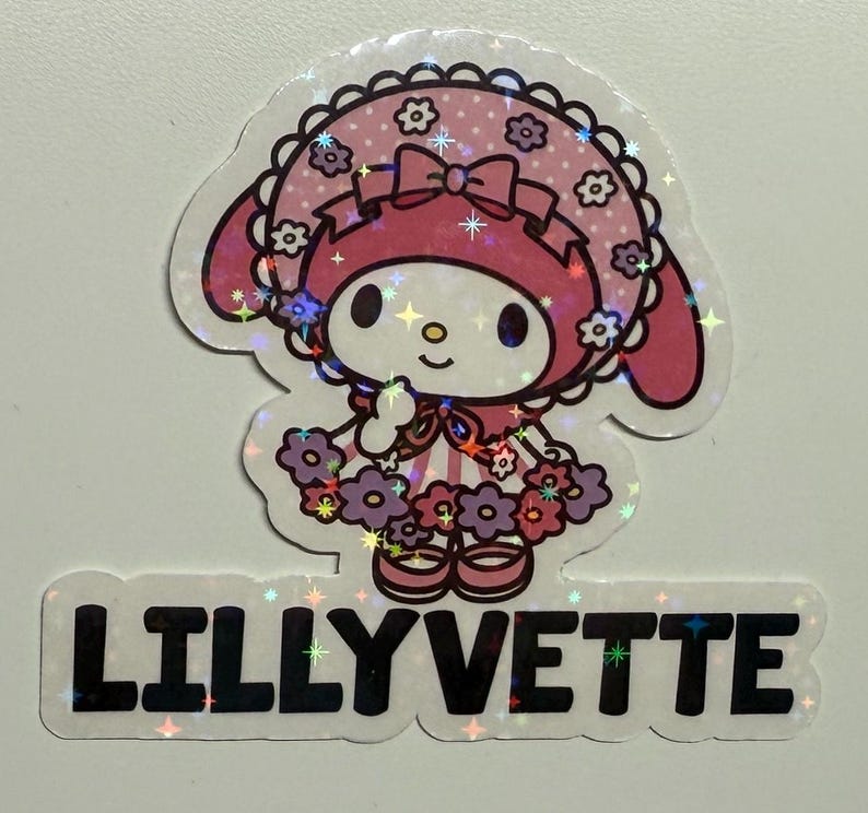 May include: A pink and white cartoon character with a pink bow and a pink and white dress with purple flowers. The character is wearing a pink and white hat with a white trim. The character is standing on a white background with the text "LILLYVETTE" in black letters.