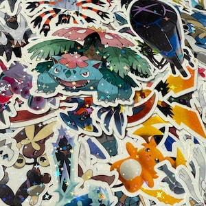 May include: A collection of colorful, holographic stickers featuring various cartoon characters. The stickers showcase a variety of designs, including a blue and green turtle-like creature with a flower on its back, and other fantasy creatures.