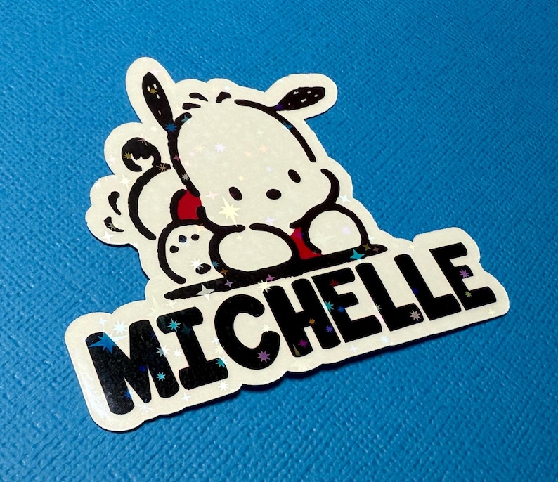 Puede incluir: Una pegatina blanca con un perro de dibujos animados en blanco y negro y el nombre "Michelle" en letras negras sobre un fondo brillante.