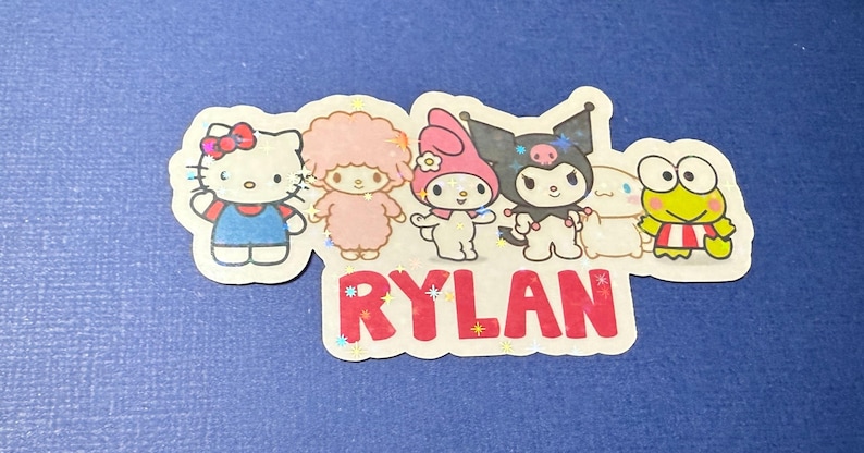 May include: A colorful sticker with five cartoon characters, including Hello Kitty, My Melody, Little Twin Stars, and Kuromi. The sticker also includes the name "RYLAN" in red letters.