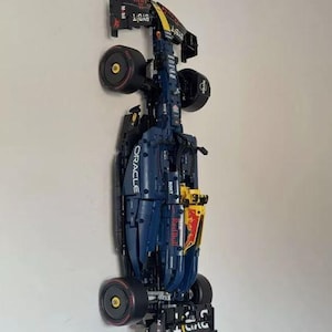 Könnte beinhalten: Ein detailliertes Modell eines Formel-1-Rennwagens, überwiegend marineblau mit roten und gelben Akzenten. Das Auto zeigt Sponsorenlogos wie Oracle, Red Bull und Bybit. Die Räder sind schwarz mit gelben und roten Details.