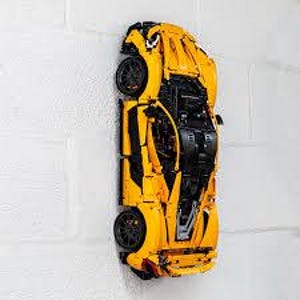 May include: A yellow and black Lego McLaren Senna model car, displayed on a white brick wall.