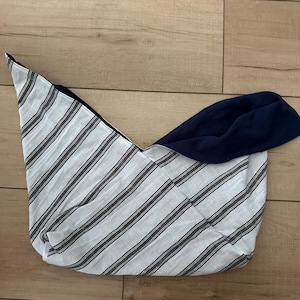 Op de afbeelding: Een omkeerbare tote bag met een gestreept patroon aan de ene kant en een effen marineblauwe stof aan de andere kant. De tas is gemaakt van een zacht, lichtgewicht materiaal en ligt op een houten oppervlak.