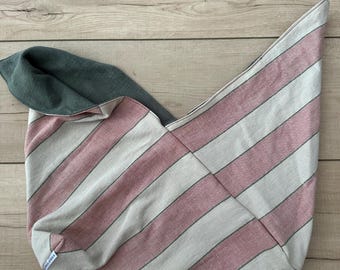 May include: A handmade tote bag with a pink and white striped pattern. The bag has a gray interior and a unique, asymmetrical shape. The fabric appears to be a soft cotton or linen blend. A small label is visible on the bottom corner.