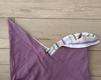 May include: A lavender-colored fabric bag with a pointed top and a striped interior. The bag is open, revealing the colorful striped lining. The bag is made of a soft, pliable material.