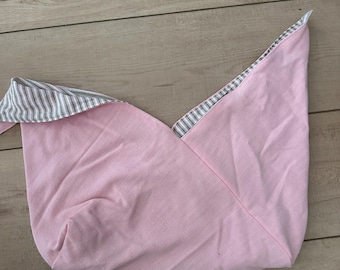 May include: A pink fabric item with a striped lining. The item is folded and appears to be a bag or pouch. The lining features thin gray and white stripes. The item is made of a soft, possibly cotton, material.