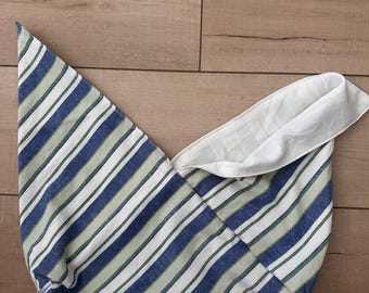 May include: A striped fabric bag with blue, green, and white stripes. The bag has a white interior and is folded over. The bag is lying on a wooden surface.