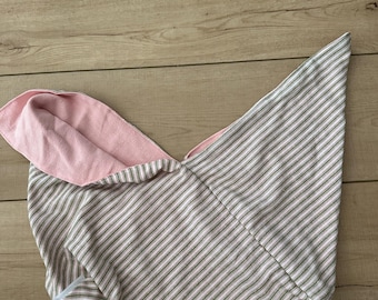 May include: A handmade, striped fabric item with a pink interior. The exterior features a pattern of thin, parallel gray and white stripes. The item is folded, revealing the pink lining. The fabric appears to be soft and likely cotton.